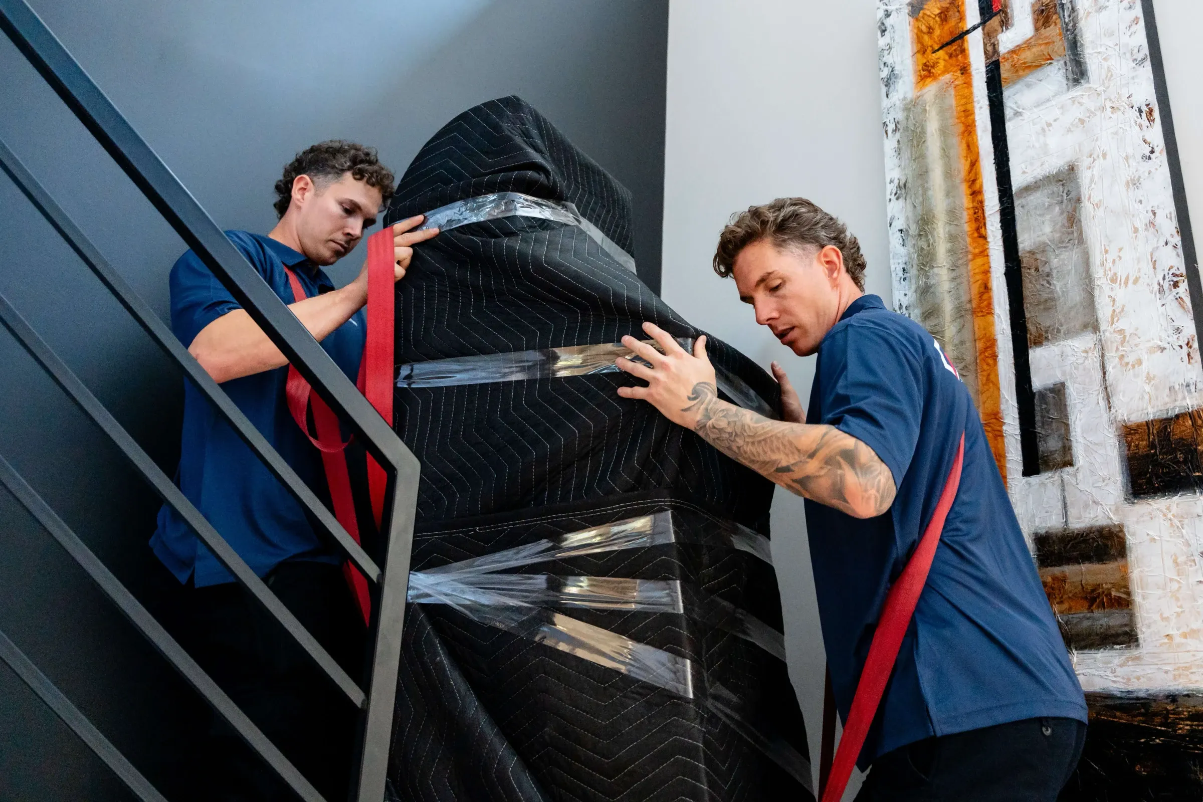 Deux déménageurs Chartrand montent un meuble emballé dans des couvertures de protection dans un escalier