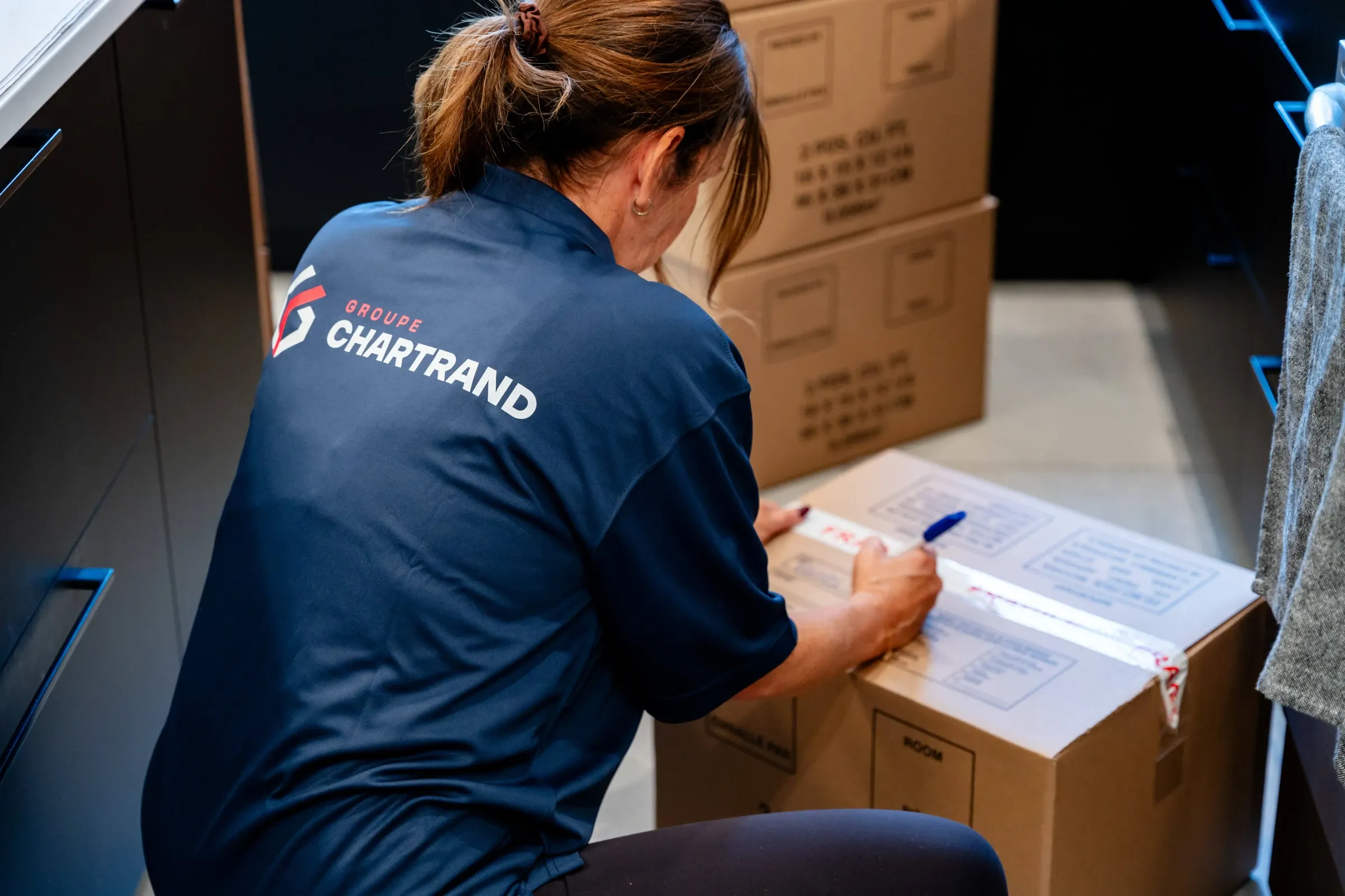 Employée Chartrand remplissant l’inventaire d’un déménagement entourée de boîtes